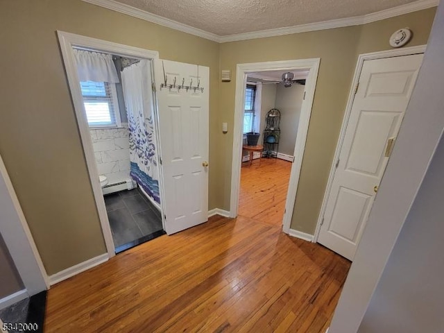 corridor with light wood-type flooring, ornamental molding, baseboard heating, and a textured ceiling