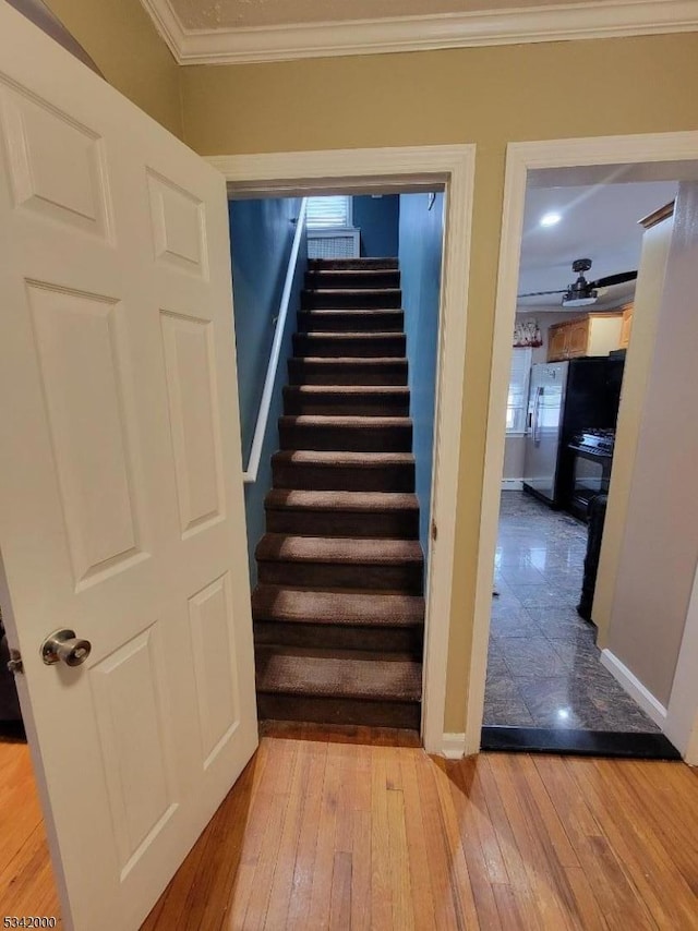 stairs featuring baseboards, wood-type flooring, and crown molding