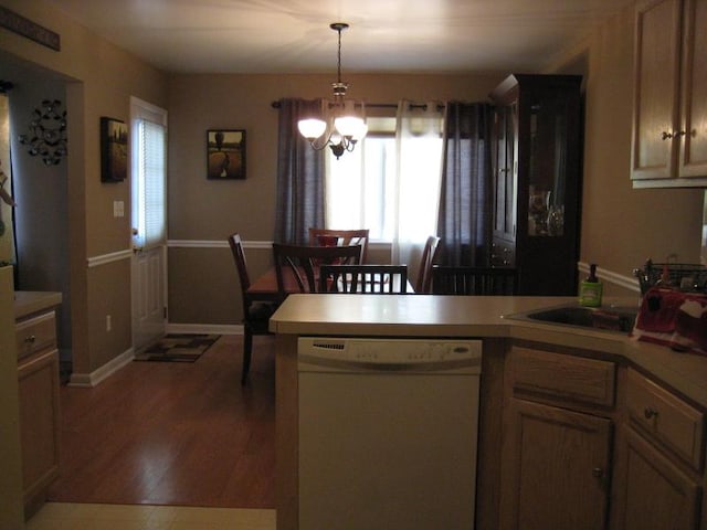 kitchen with wood finished floors, a peninsula, white dishwasher, light countertops, and a chandelier