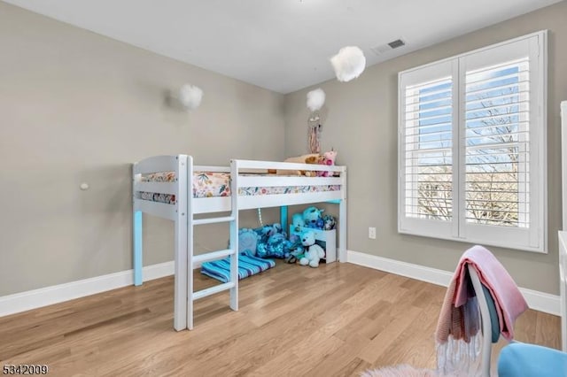 bedroom featuring baseboards, multiple windows, visible vents, and wood finished floors