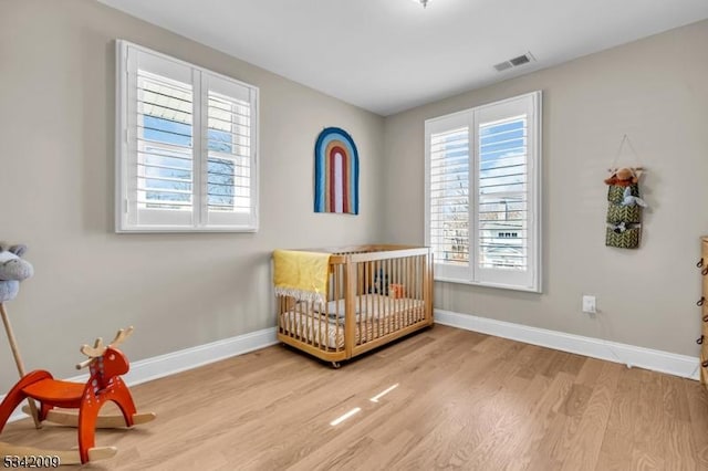 bedroom with a crib, visible vents, baseboards, and wood finished floors