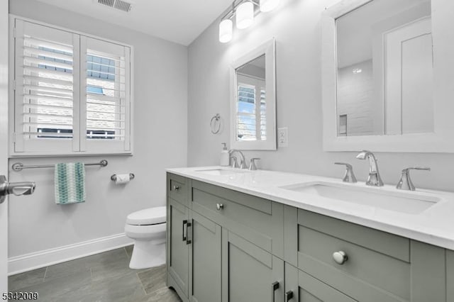 bathroom featuring toilet, double vanity, visible vents, and a sink