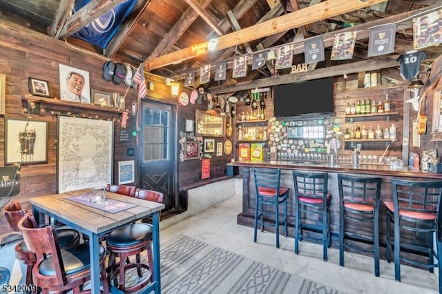 bar with lofted ceiling, concrete floors, a dry bar, and wood walls