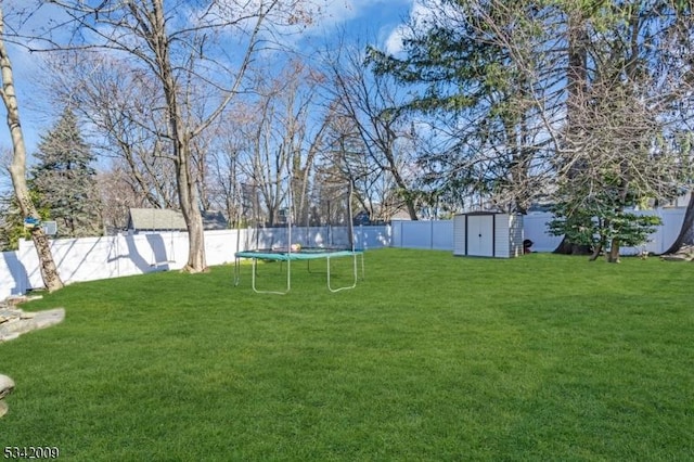 view of yard featuring a trampoline, an outbuilding, a fenced backyard, and a storage shed