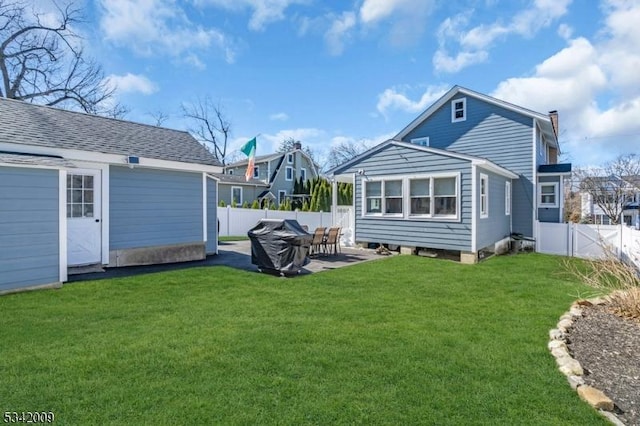 rear view of house featuring a lawn, a patio, a fenced backyard, roof with shingles, and an outdoor structure