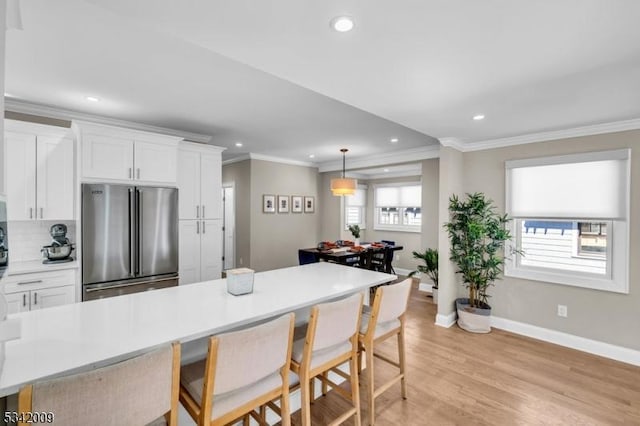 kitchen with a healthy amount of sunlight, white cabinets, a kitchen breakfast bar, and freestanding refrigerator