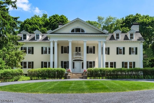 neoclassical / greek revival house featuring a chimney, a front lawn, and stucco siding