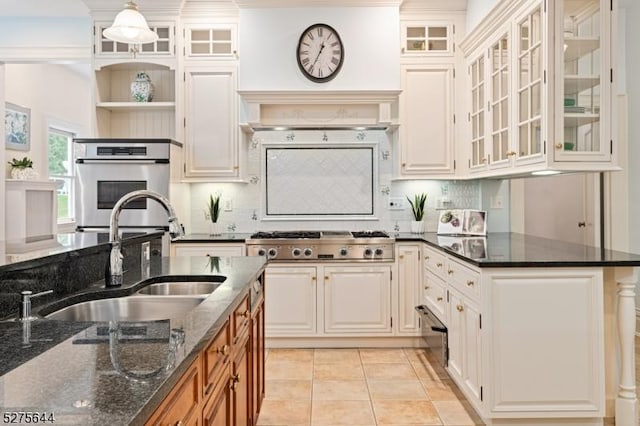 kitchen with light tile patterned floors, backsplash, appliances with stainless steel finishes, a sink, and dark stone counters