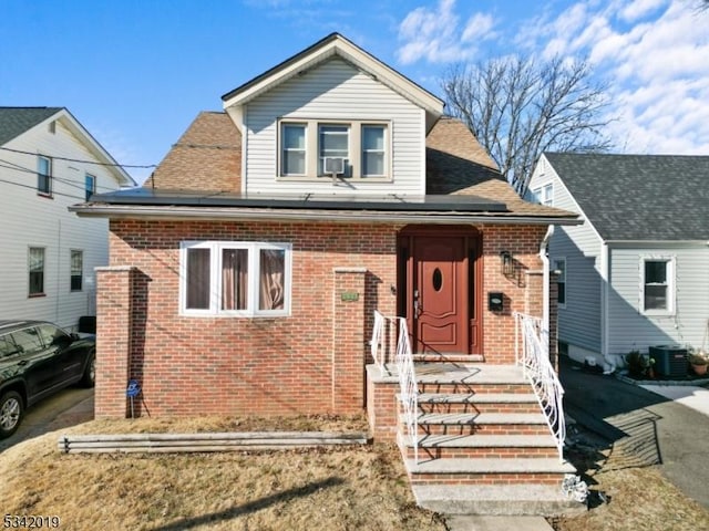 bungalow-style house featuring brick siding, roof with shingles, cooling unit, and roof mounted solar panels