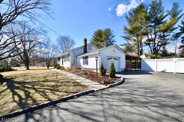 view of home's exterior featuring aphalt driveway, fence, a garage, and a chimney