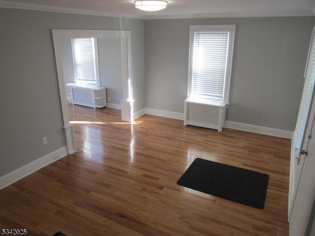 empty room featuring radiator, baseboards, crown molding, and wood finished floors