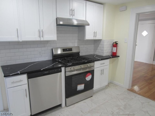 kitchen featuring marble finish floor, dark countertops, appliances with stainless steel finishes, white cabinetry, and under cabinet range hood