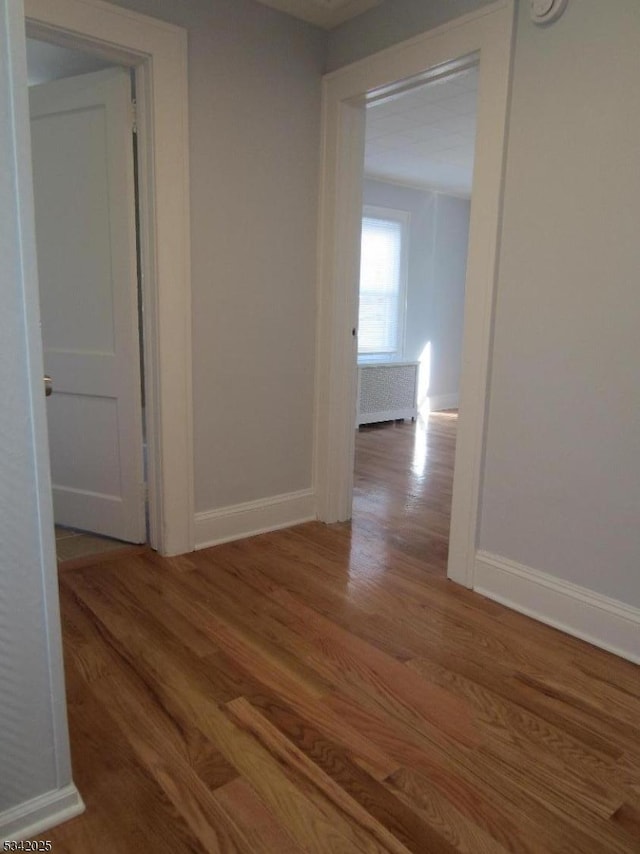 corridor featuring baseboards, radiator heating unit, and wood finished floors