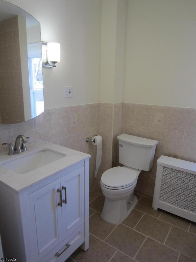 half bathroom featuring radiator, toilet, tile patterned flooring, vanity, and tile walls