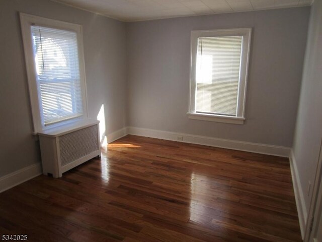 unfurnished room with baseboards, wood finished floors, and radiator