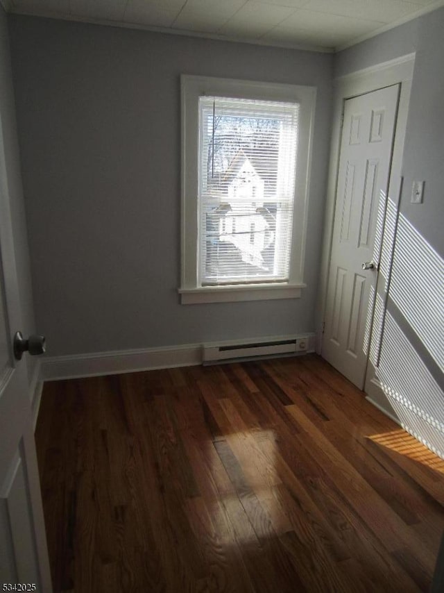 empty room featuring dark wood-style floors, a baseboard radiator, and baseboards