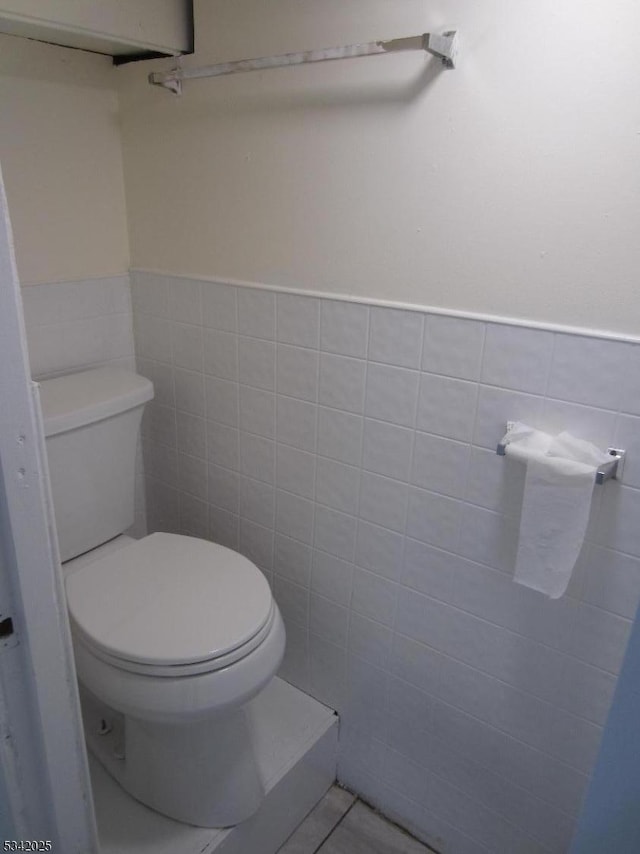 bathroom with toilet, a wainscoted wall, tile patterned flooring, and tile walls