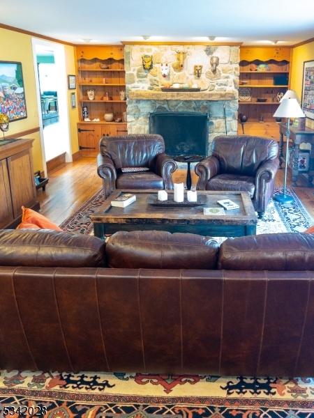 living area featuring a stone fireplace, built in shelves, wood finished floors, and ornamental molding