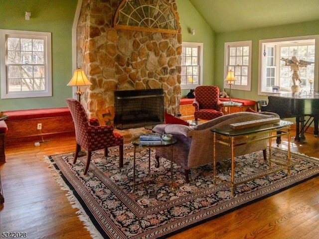 sitting room with a stone fireplace, lofted ceiling, and wood finished floors