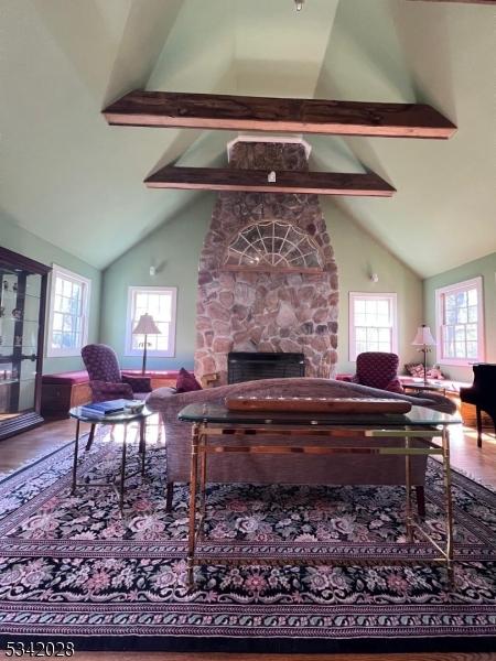 living area featuring beamed ceiling, high vaulted ceiling, a stone fireplace, and wood finished floors