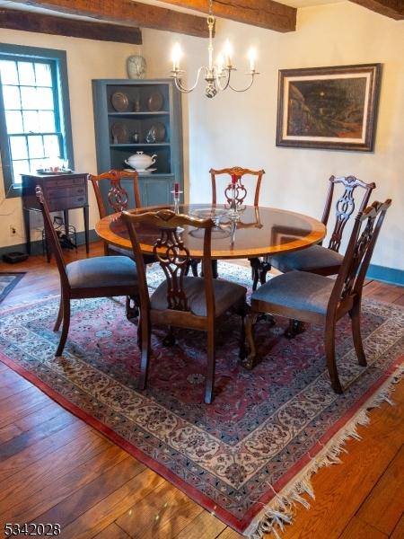 dining area with baseboards, wood-type flooring, a notable chandelier, and beamed ceiling