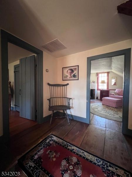 hall featuring visible vents, baseboards, and wood-type flooring