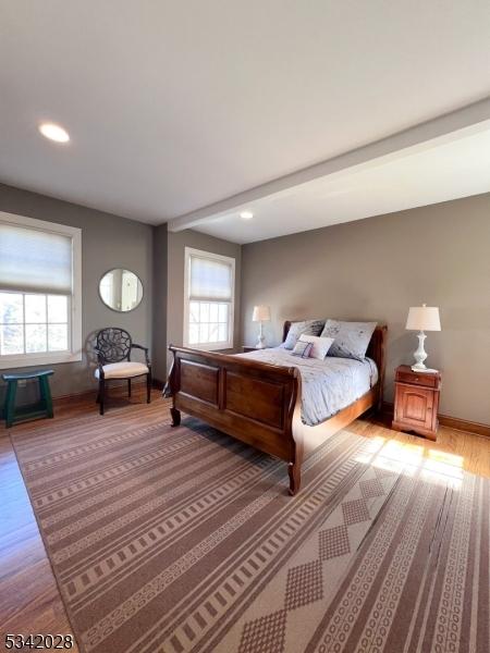 bedroom featuring light wood-type flooring, multiple windows, baseboards, and beamed ceiling