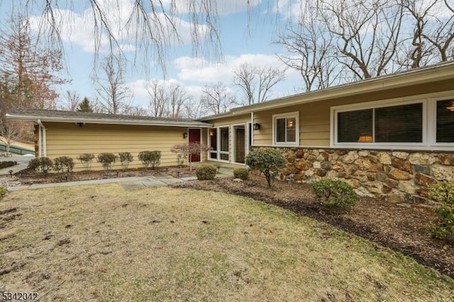 back of house with stone siding and a lawn