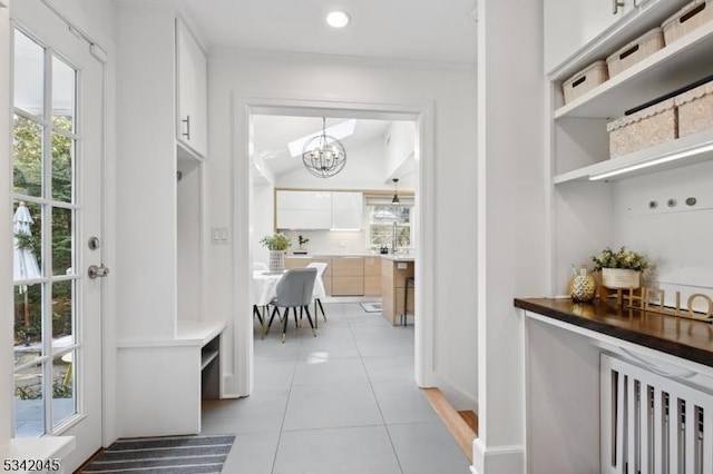 mudroom with ornamental molding, light tile patterned flooring, and an inviting chandelier