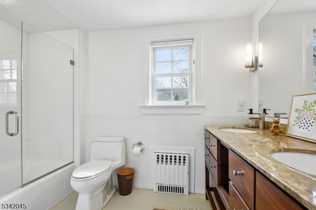 full bath with toilet, radiator heating unit, double vanity, and a sink