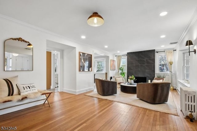 living area with crown molding, radiator, visible vents, wood-type flooring, and a tiled fireplace