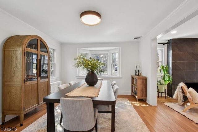 dining area featuring light wood-type flooring, a tile fireplace, visible vents, and crown molding