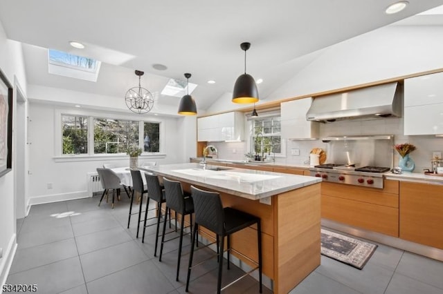 kitchen with stainless steel gas cooktop, vaulted ceiling with skylight, modern cabinets, and range hood