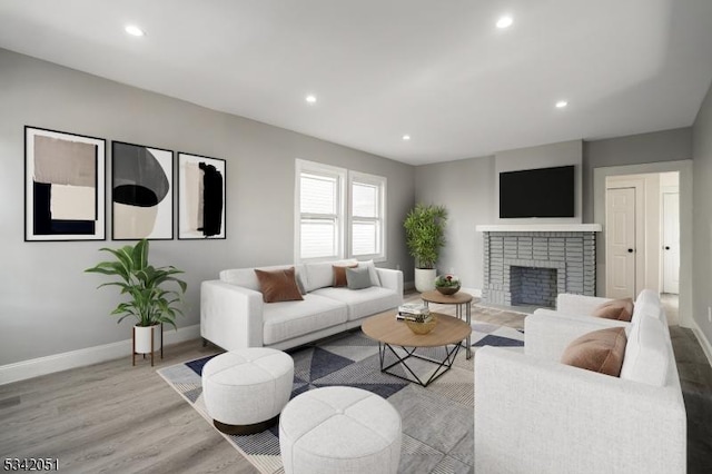 living room with light wood-style floors, recessed lighting, a brick fireplace, and baseboards