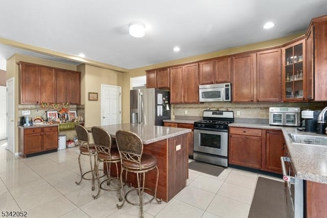 kitchen with brown cabinetry, light tile patterned flooring, stainless steel appliances, a kitchen breakfast bar, and a center island