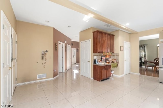 kitchen featuring tasteful backsplash, visible vents, light tile patterned floors, and brown cabinets