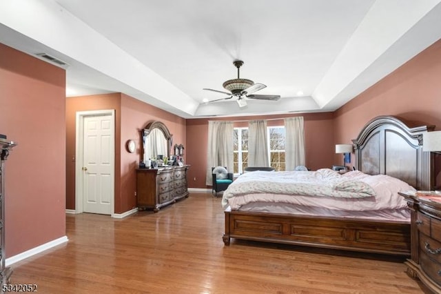 bedroom featuring light wood-type flooring, visible vents, a ceiling fan, baseboards, and a raised ceiling