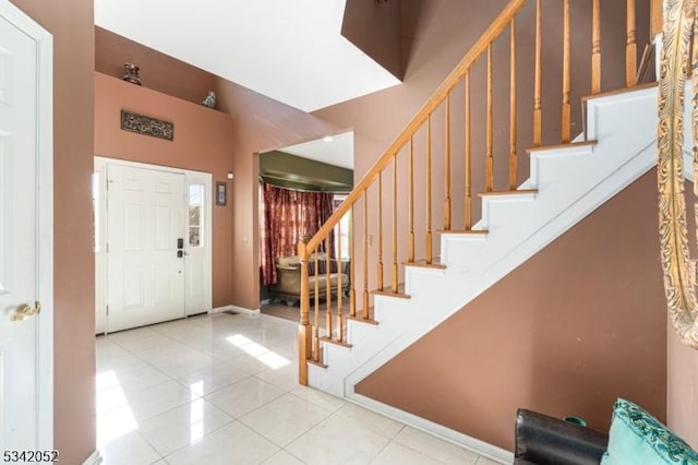 tiled entrance foyer featuring stairway, baseboards, and a towering ceiling