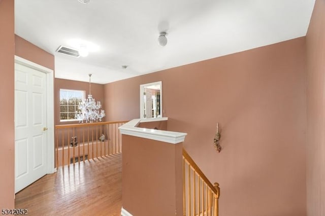 hall featuring visible vents, an upstairs landing, light wood-style floors, and a chandelier