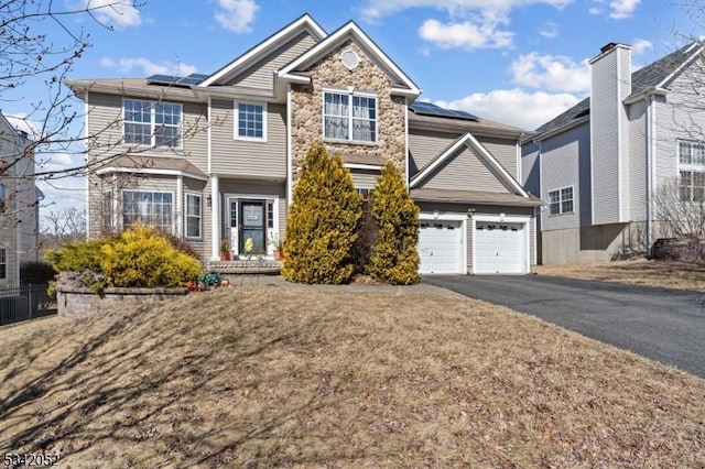 view of front of house with solar panels, a garage, stone siding, and driveway