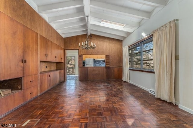 kitchen featuring a healthy amount of sunlight, lofted ceiling with beams, refrigerator, wood walls, and a chandelier