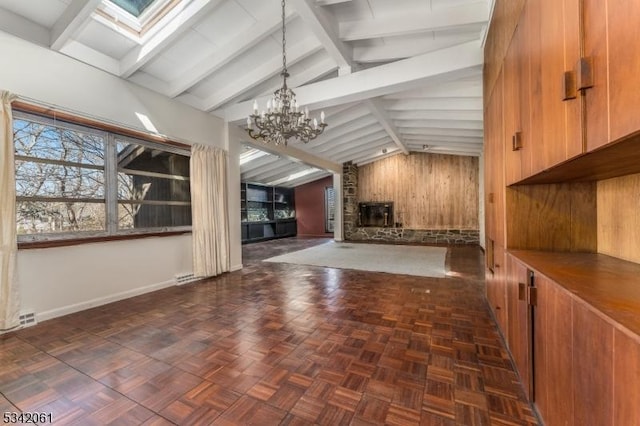 unfurnished living room featuring lofted ceiling with skylight, a notable chandelier, wood walls, and a healthy amount of sunlight