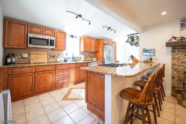 kitchen featuring a kitchen breakfast bar, brown cabinetry, tasteful backsplash, and stainless steel appliances