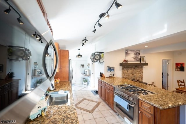 kitchen featuring light stone counters, appliances with stainless steel finishes, wall chimney exhaust hood, brown cabinetry, and light tile patterned floors