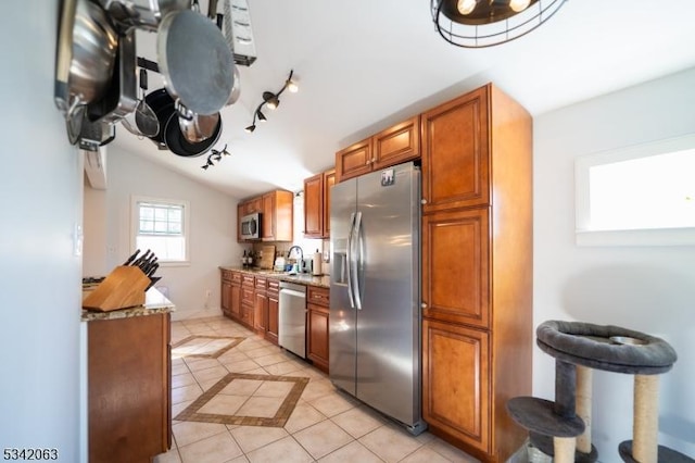 kitchen featuring vaulted ceiling, light tile patterned floors, brown cabinets, stainless steel appliances, and a sink