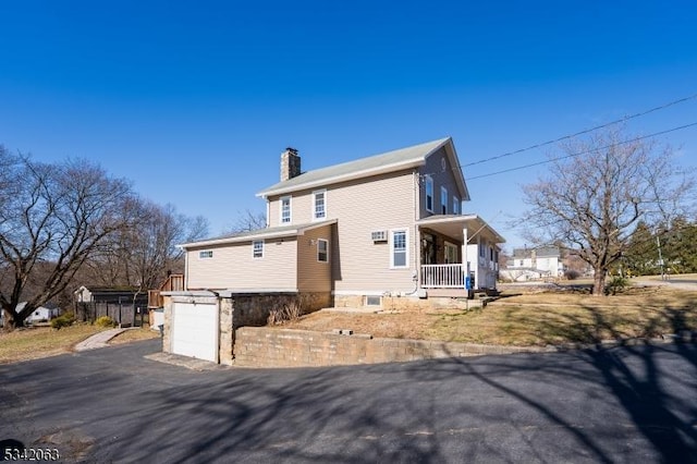 view of front of home with a porch, a chimney, driveway, and an attached garage