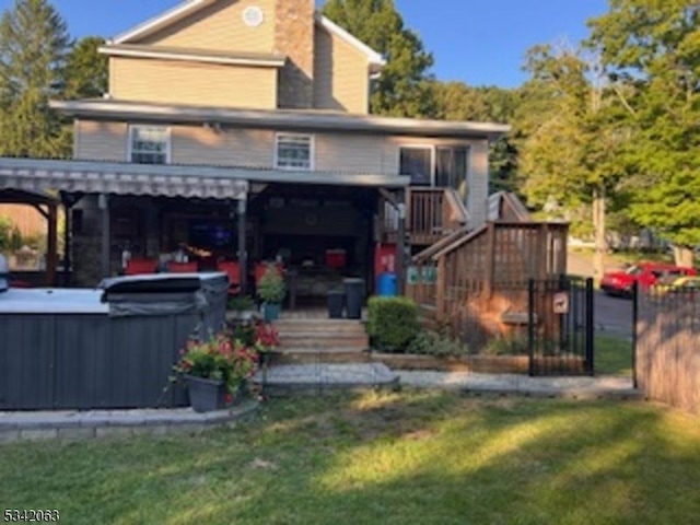 rear view of house with stairs, a yard, a chimney, and a hot tub