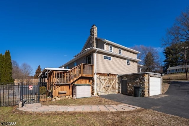 rear view of house with an outbuilding, aphalt driveway, fence, a garage, and a chimney