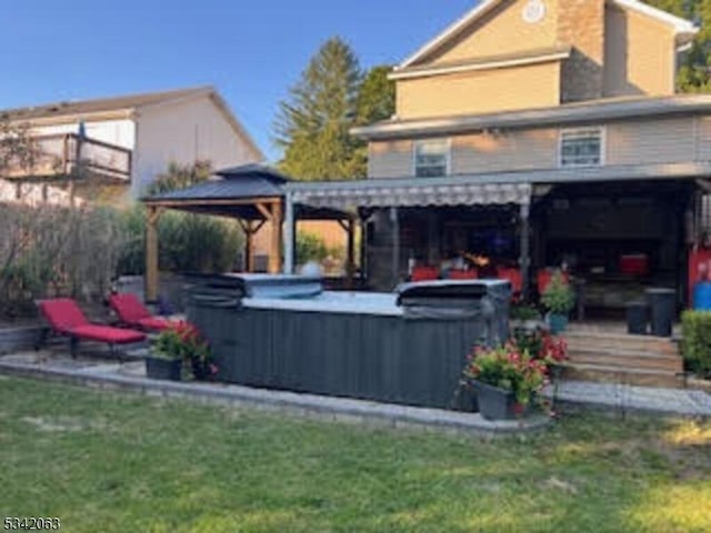 rear view of property featuring a gazebo, a yard, and a hot tub