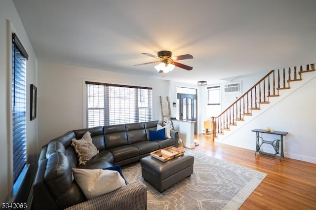 living room featuring an AC wall unit, a ceiling fan, wood finished floors, stairway, and baseboards